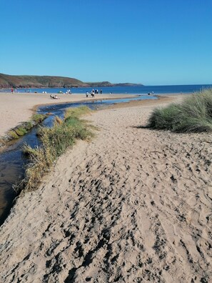 Ein sandiger Strand mit einem Bach, Menschen, die spazieren gehen, und Zelte in der Ferne.