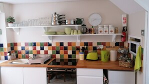 Una cocina con gabinetes blancos, un salpicadero de azulejos coloridos y diversos electrodomésticos y utensilios de cocina sobre la encimera.