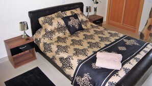 Un lit bien fait, recouvert d’une couvre-lit à motifs, une table de chevet avec une lampe et un petit vase avec des fleurs.