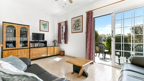 Een woonkamer met een bank, een salontafel, een televisie, een kast en een schuifdeur naar een buitenruimte.