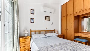 Een slaapkamer met een bed, een houten kledingkast, nachtkastje en een raam met gordijnen.