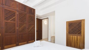 Une chambre avec une grande armoire en bois, un lit recouvert d’une couette blanche et un panier en osier.