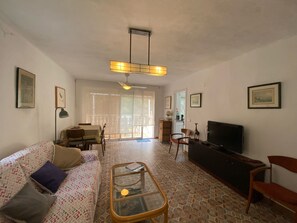 Una sala de estar con un sofá, una mesa de centro de vidrio, un televisor y un comedor con sillas.