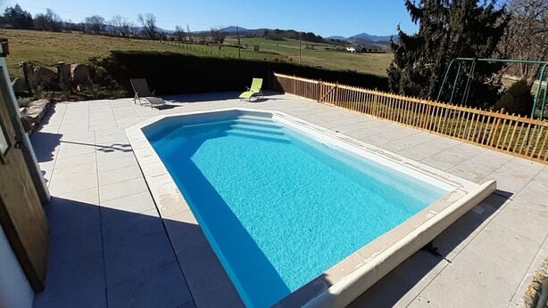 Una piscina rectangular con superficie de agua azul cristalina, rodeada por una terraza de baldosas.