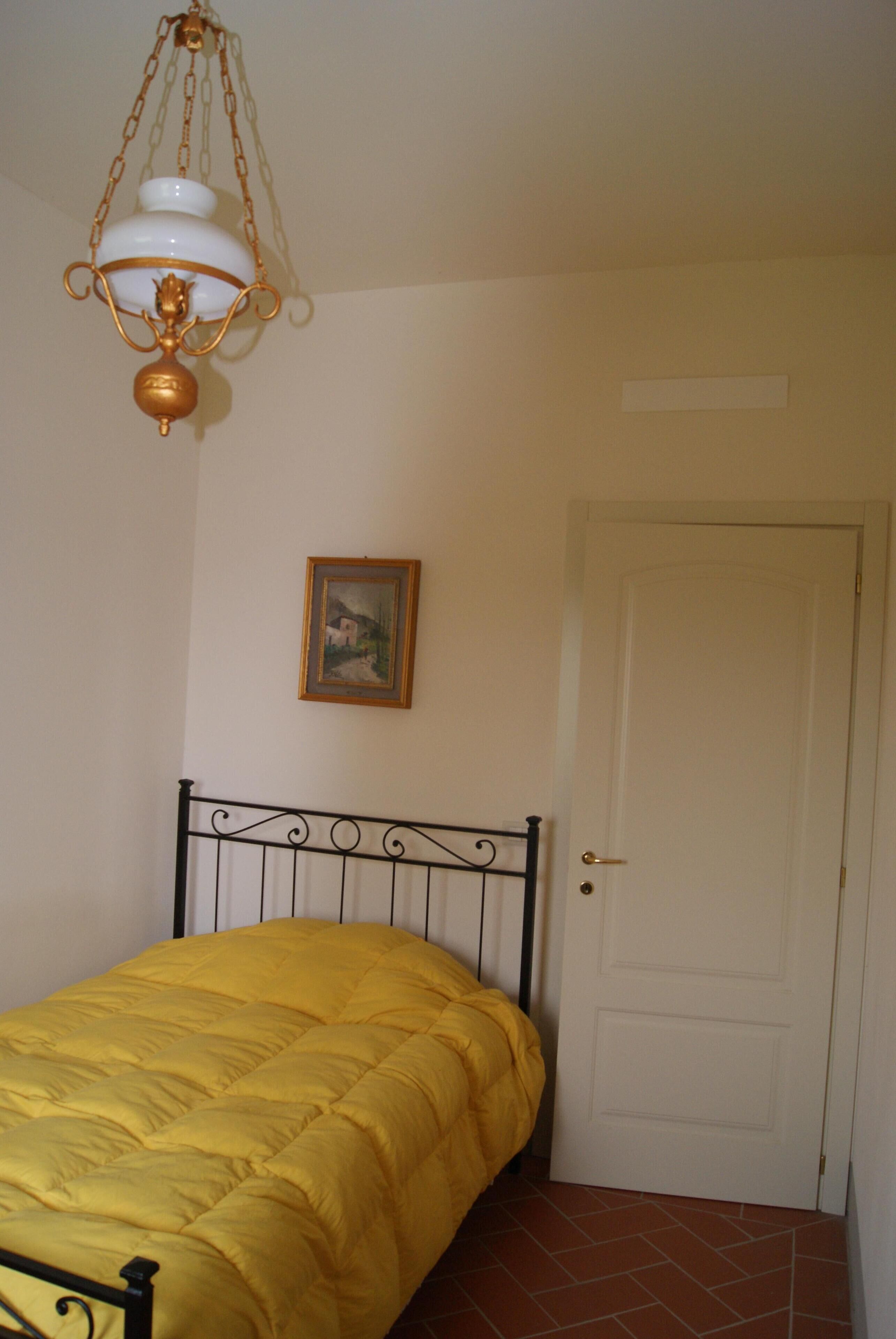 Ein Schlafzimmer mit einem Bett, einer Tür, einem gerahmten Bild an der Wand und einer Hängeleuchte.