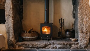 A stone fireplace with a black stove, a basket, and a kettle. - Remote Cottage with Woodburner Surrounded by Farmland  (Redruth)