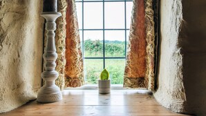 A rustic room with a wooden ceiling, a window with patterned curtains, and a candle holder on a wooden ledge. - Remote Cottage with Woodburner Surrounded by Farmland  (Redruth)