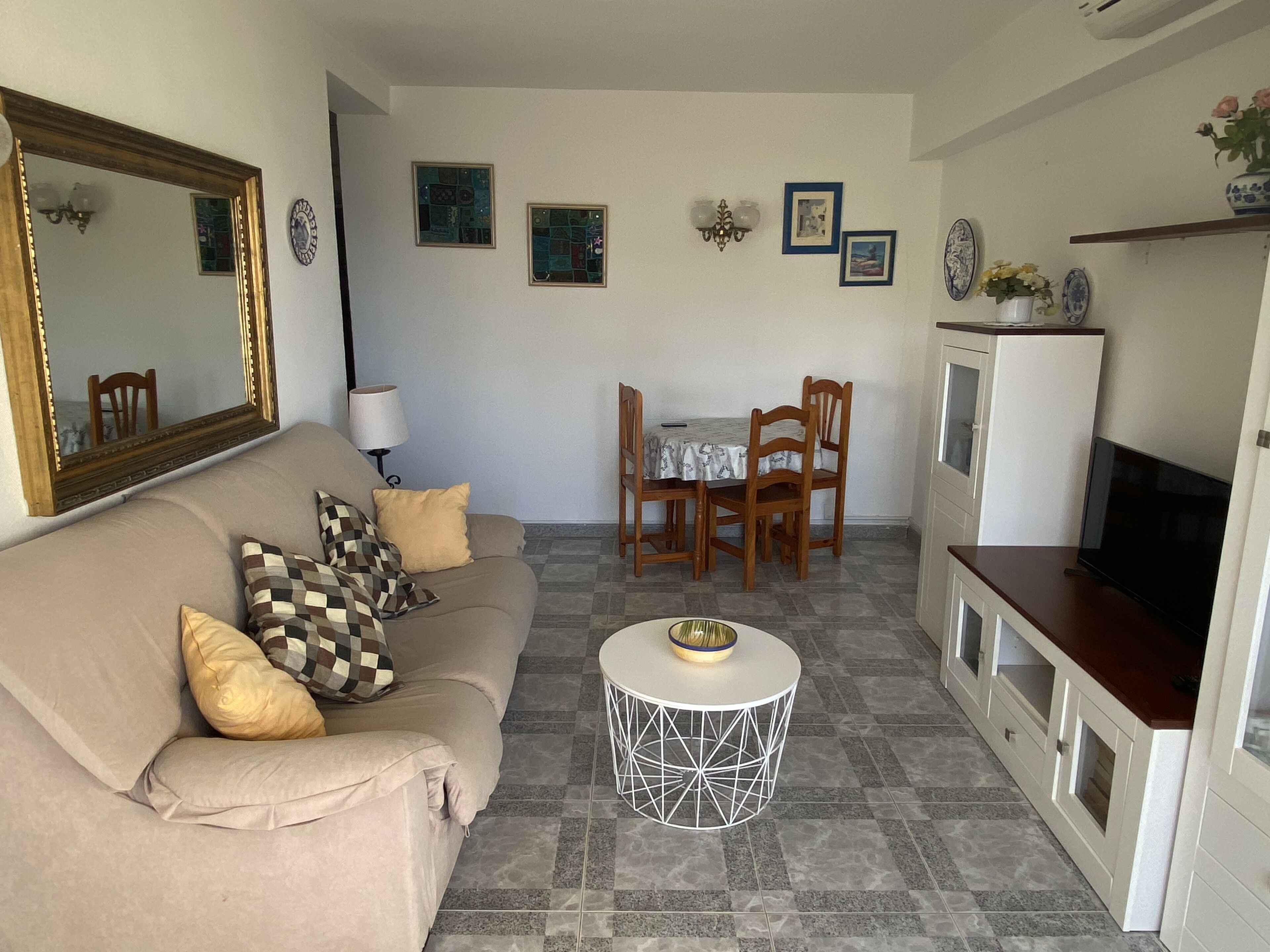 A living room with a sofa, a coffee table, a dining table with chairs, a TV, and a refrigerator.