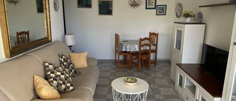 A living room with a sofa, a coffee table, a dining table with chairs, a TV, and a refrigerator.