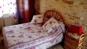 A bedroom with a stone wall, a wooden bed frame, floral bedding, a wicker nightstand, and a red lamp. - Au Calme Stone house, large pool. near sea1,.5 km classified 4 stars (Saint-Pierre-D'oléron)