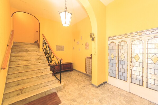 A staircase with a wooden handrail and a metal balustrade, leading to a landing with a bench and a wall-mounted light fixture.