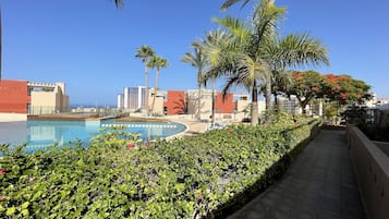 Zona de piscina con vista despejada al océano, rodeada de palmeras y edificios modernos.