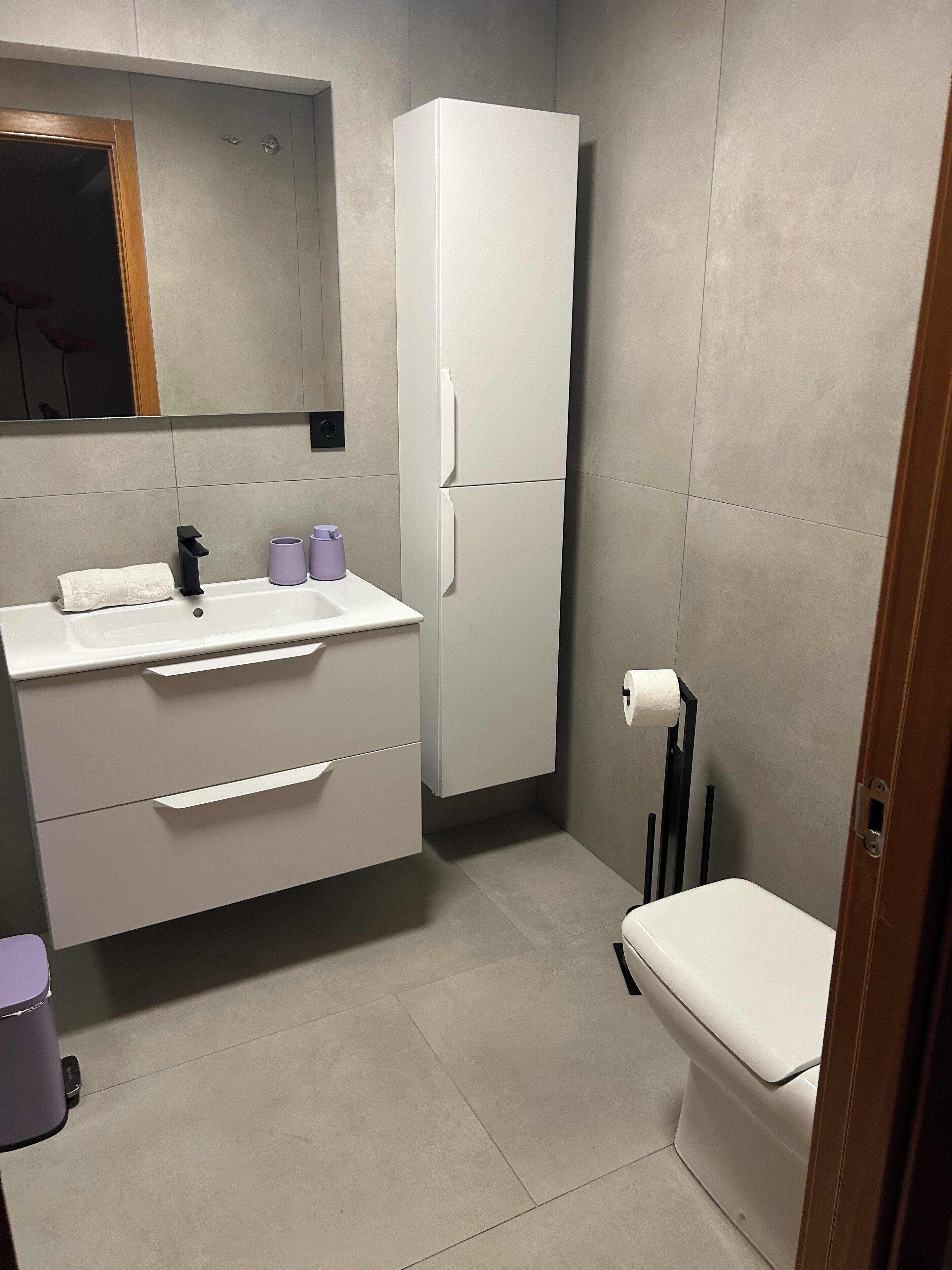 Un baño moderno con un tocador blanco, un inodoro y un espejo grande.