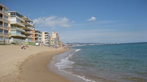 Una playa con una hilera de edificios de varios pisos, algunos con balcones, y una vista despejada del mar.