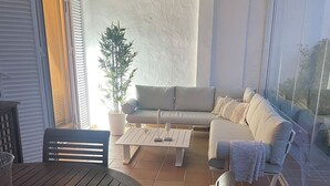 Eine sonnendurchflutete Terrasse mit Holztisch und -stühlen, einer Couch und einem Blumentopf.