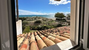 Blick aus einem Fenster auf Küstenterrassen mit roten Ziegeldächern, einen Sandstrand und das Meer.