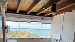 Ein Schlafzimmer mit großem Fenster mit Blick auf den Strand, einem Bett, einem Schreibtisch und einem Stuhl.
