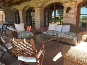 A covered patio area with wicker furniture, a glass table, and brick walls.