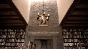 Una biblioteca con chimenea de piedra, estanterías de madera y una lámpara colgante.