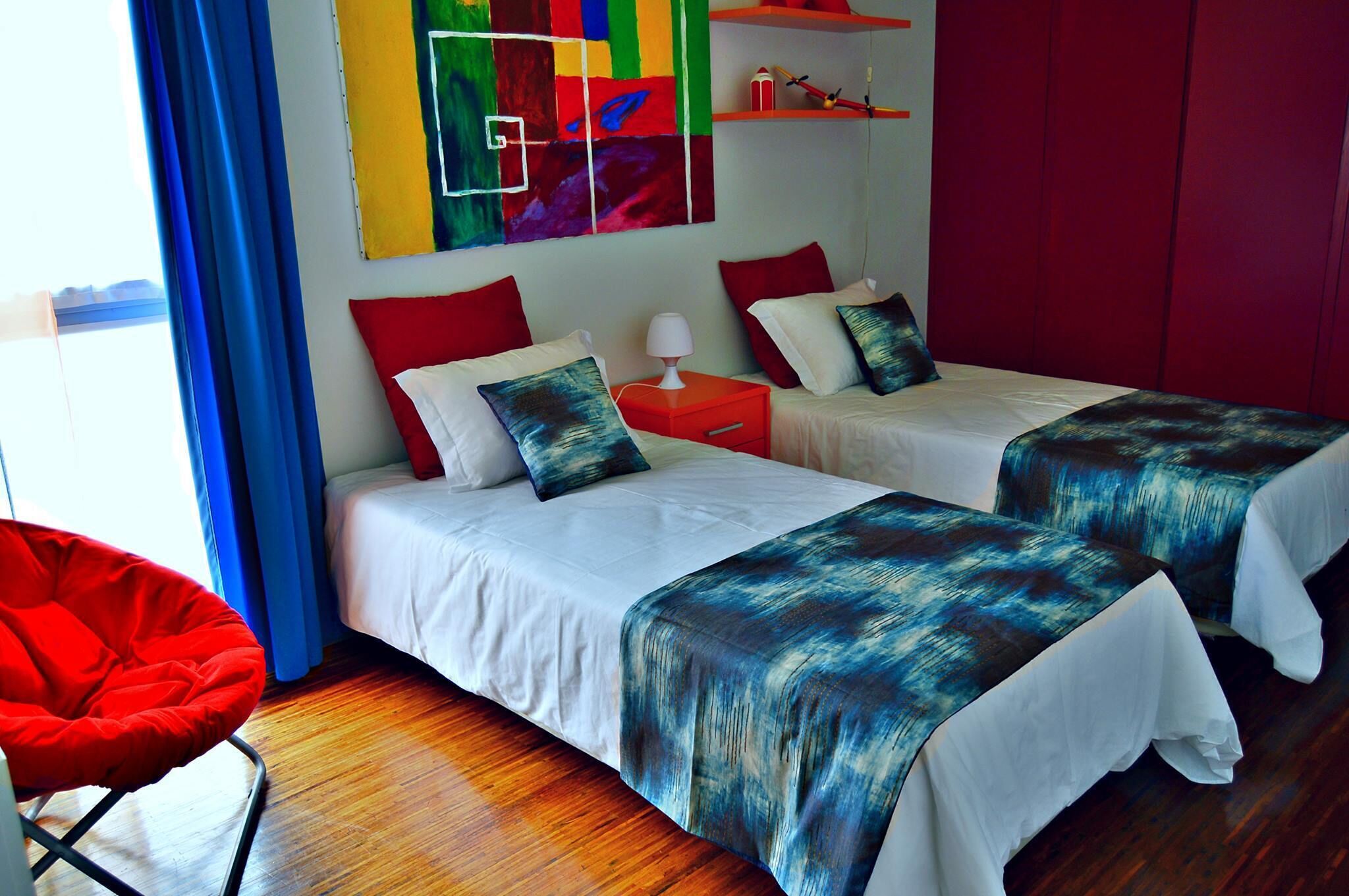 A hotel room with two beds, a red chair, and a colorful abstract painting on the wall.