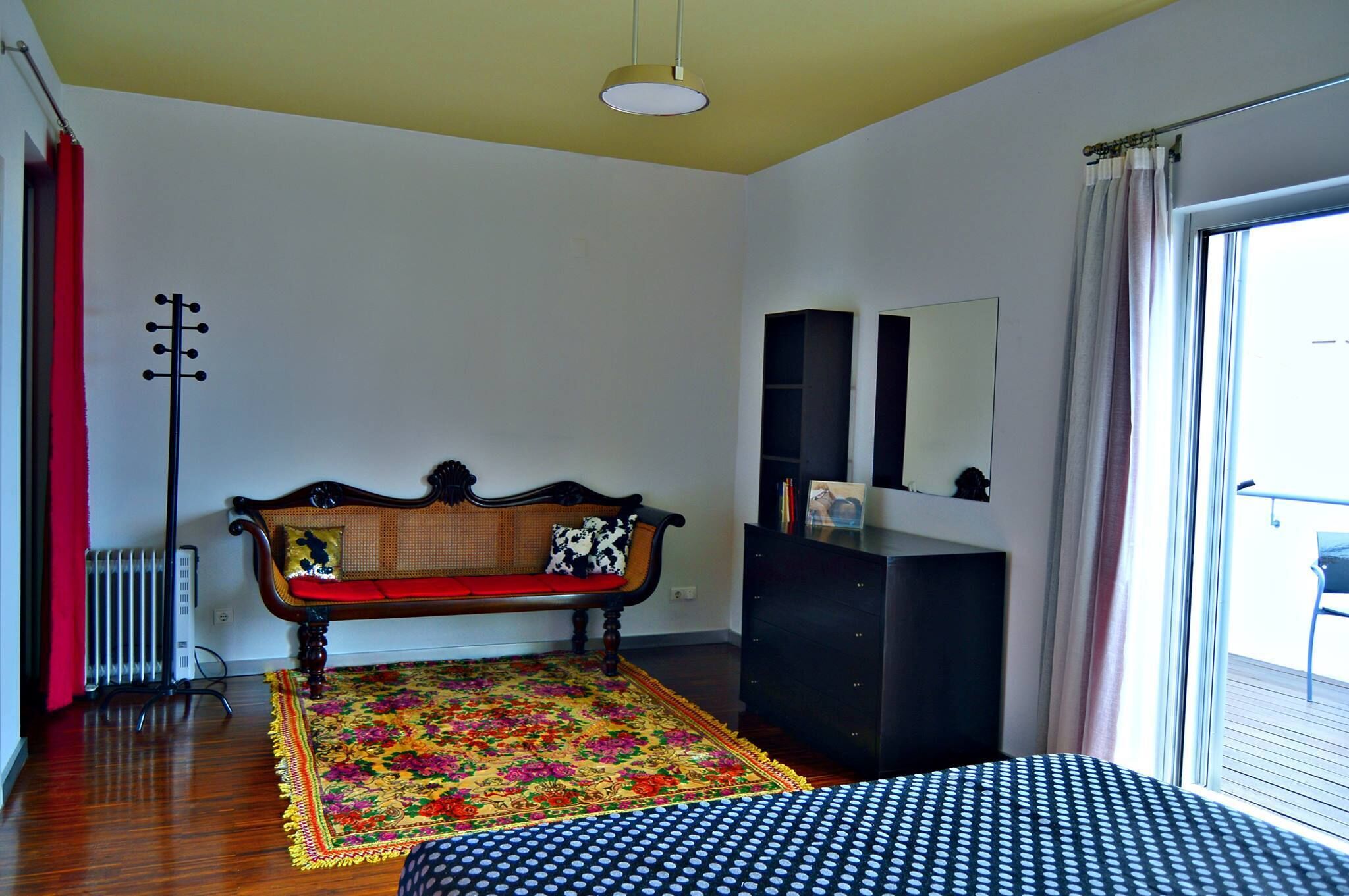 Ein Zimmer mit einer hölzernen Bank, einem schwarzen Schrank, einem großen Spiegel und einem farbenfrohen Teppich.