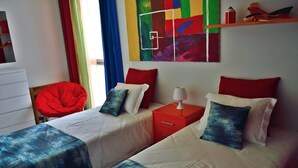 Ein Hotelzimmer mit zwei Betten, einem roten Sessel, einem farbenfrohen abstrakten Gemälde und einem Regal mit Dekorationen.