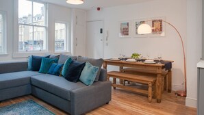 Ein modernes Wohnzimmer mit einem grauen Ecksofa, einem Holzessttisch und einem großen Fenster.
