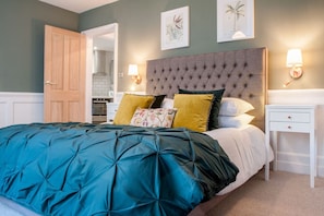 Une chambre à coucher avec une tête de lit capitonnée, une couette turquoise et une table de chevet blanche avec une lampe.