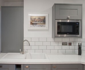 Una cocina con un microondas de acero inoxidable, un lavabo con un grifo moderno y un cuadro enmarcado de un paisaje urbano.