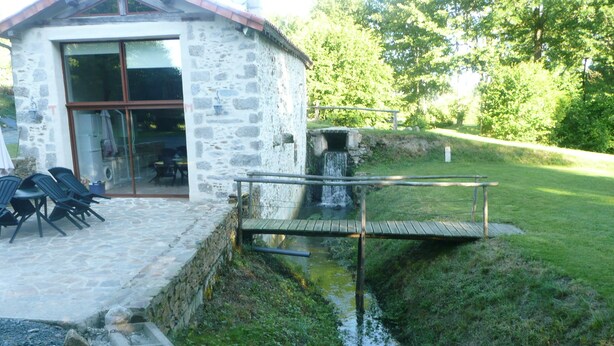 Un edificio de piedra con puerta de vidrio, mesas al aire libre y una pequeña fuente.