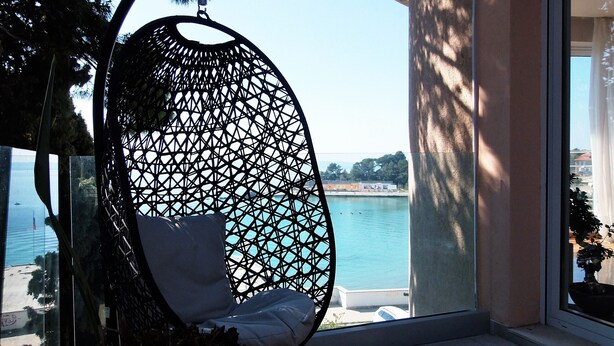A hanging chair with a geometric pattern, overlooking a body of water and a distant shoreline. - Splendid Apartment right next to a sandy beach (Split)