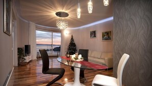 A modern dining area with a glass table, black and white chairs, a Christmas tree, and a view of the sunset through large windows. - Splendid Apartment right next to a sandy beach (Split)