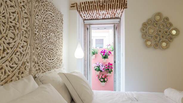 A bedroom with two beds, a decorative headboard, a hanging light fixture, and a view of a pink wall with flowers.