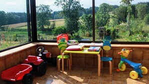 A room with a large window overlooking a green landscape, a wooden table with toys, and a red toy car.