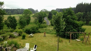 A grassy outdoor area with a picnic table and chairs, a swing set, and a view of a road in the distance.