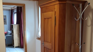 Une armoire en bois avec un porte-manteau, un banc en bois avec un coussin, et une porte donnant sur une autre pièce.
