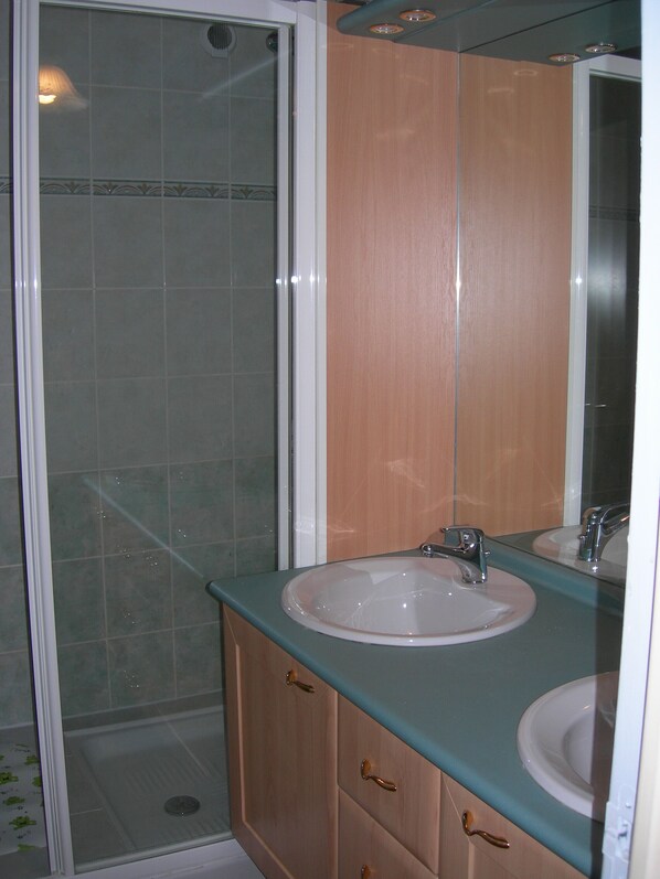 A bathroom with a glass shower enclosure, a sink with a mirror, and wooden cabinets.