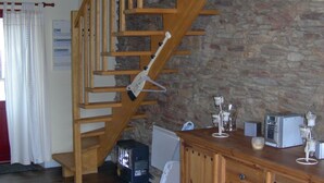 Una escalera de madera con un fondo de pared de piedra, un armario de madera con cajones y una pequeña cocina con electrodomésticos.