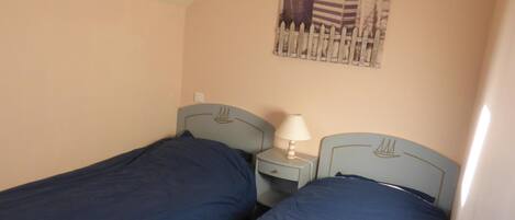 Une chambre avec deux lits simples, une table de chevet avec une lampe et une affiche accrochée au mur.
