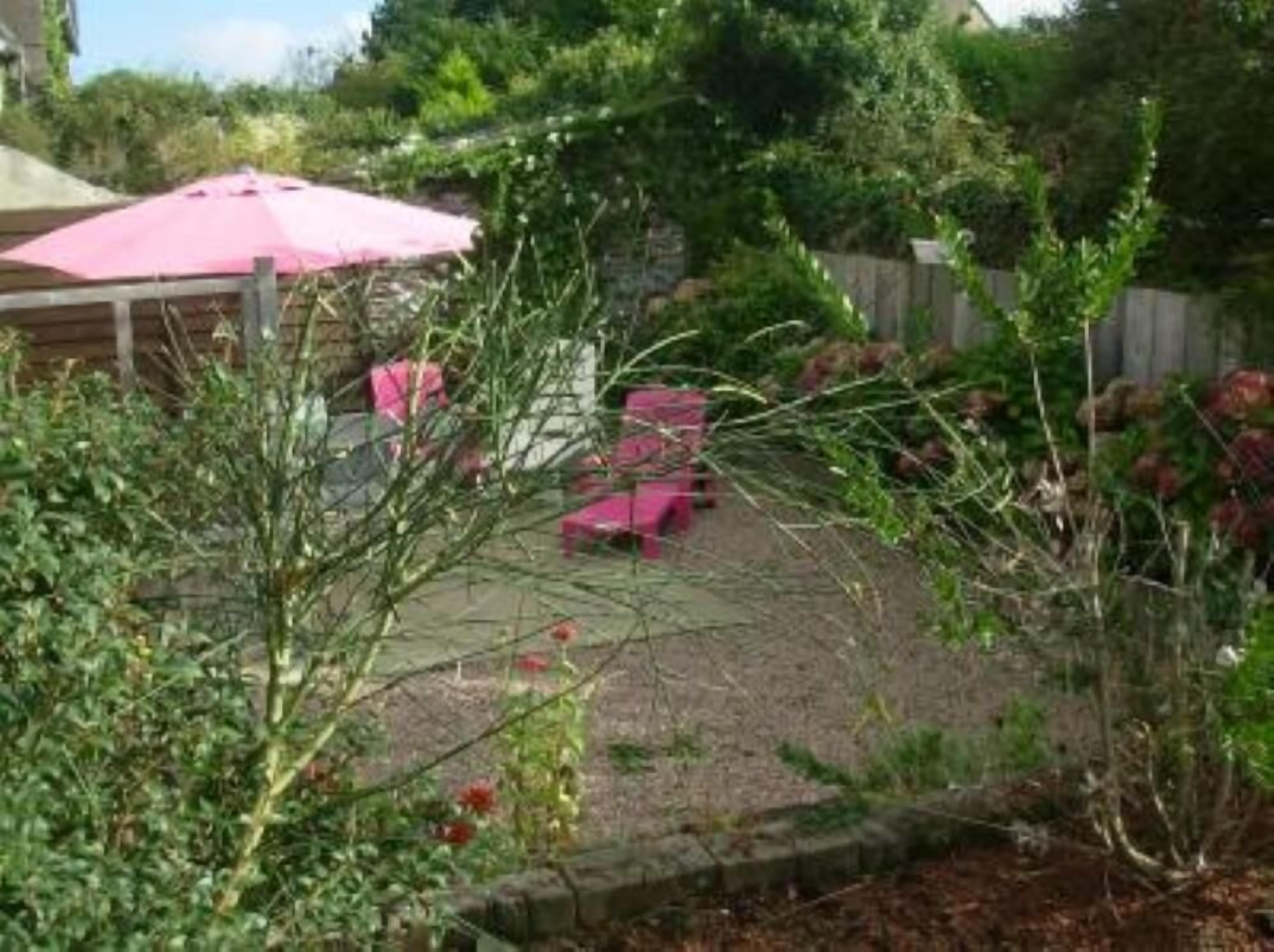 Un espace jardin agrémenté d’un parasol rose, d’une clôture en bois et d’une terrasse avec des chaises roses.