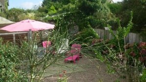 Un jardín con sombrilla rosa, valla de madera y patio con sillas rosadas.