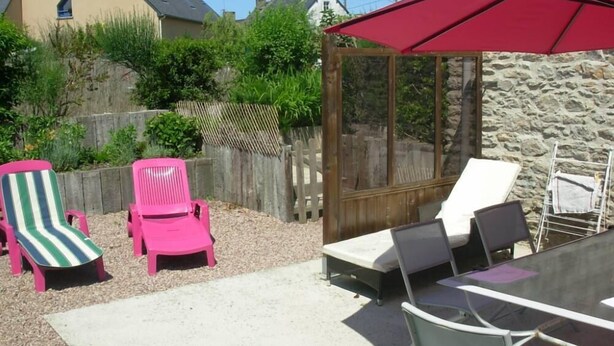 Un patio exterior con una mesa, sillas, un paraguas rojo y una valla de madera.