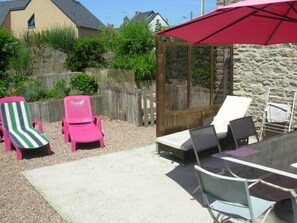 An outdoor patio with a table and chairs, a red umbrella, and a wooden fence.