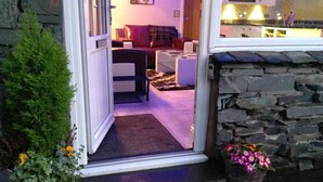 A cozy living room with a sofa and coffee table, a stone wall, and a door leading to the outside. - Stylish & Contemporary 5 * Fully Renovated Luxurious Holiday Cottage Ambleside  (Ambleside)