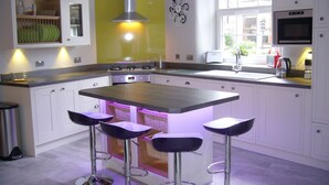 A modern kitchen with a central island, bar stools, a stainless steel range hood, and a window providing natural light. - Stylish & Contemporary 5 * Fully Renovated Luxurious Holiday Cottage Ambleside  (Ambleside)