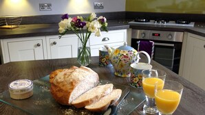A kitchen counter with a loaf of bread, a teapot, a vase with flowers, and glasses of orange juice. - Stylish & Contemporary 5 * Fully Renovated Luxurious Holiday Cottage Ambleside  (Ambleside)