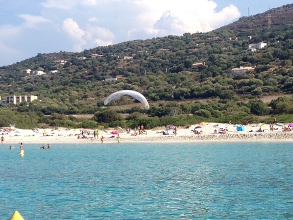 A beach with people, a parasail, and buildings on a hillside. - T3, 350 m from the Bodri BEACH, Sea view, Air-conditioned, Landscaped and enclosed park. (Corbara)