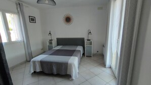 Une chambre à coucher comprenant un lit, deux tables de chevet, un luminaire fixé au mur et une fenêtre avec des rideaux.
