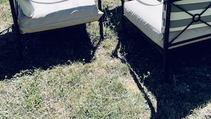 Un jardin agrémenté de deux chaises longues et d’une table en pierre, offrant une vue sur un paysage montagneux.