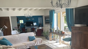 Un salon spacieux avec un canapé, une table basse et un téléviseur. Au fond, on aperçoit un coin cuisine avec une table à manger et des chaises.
